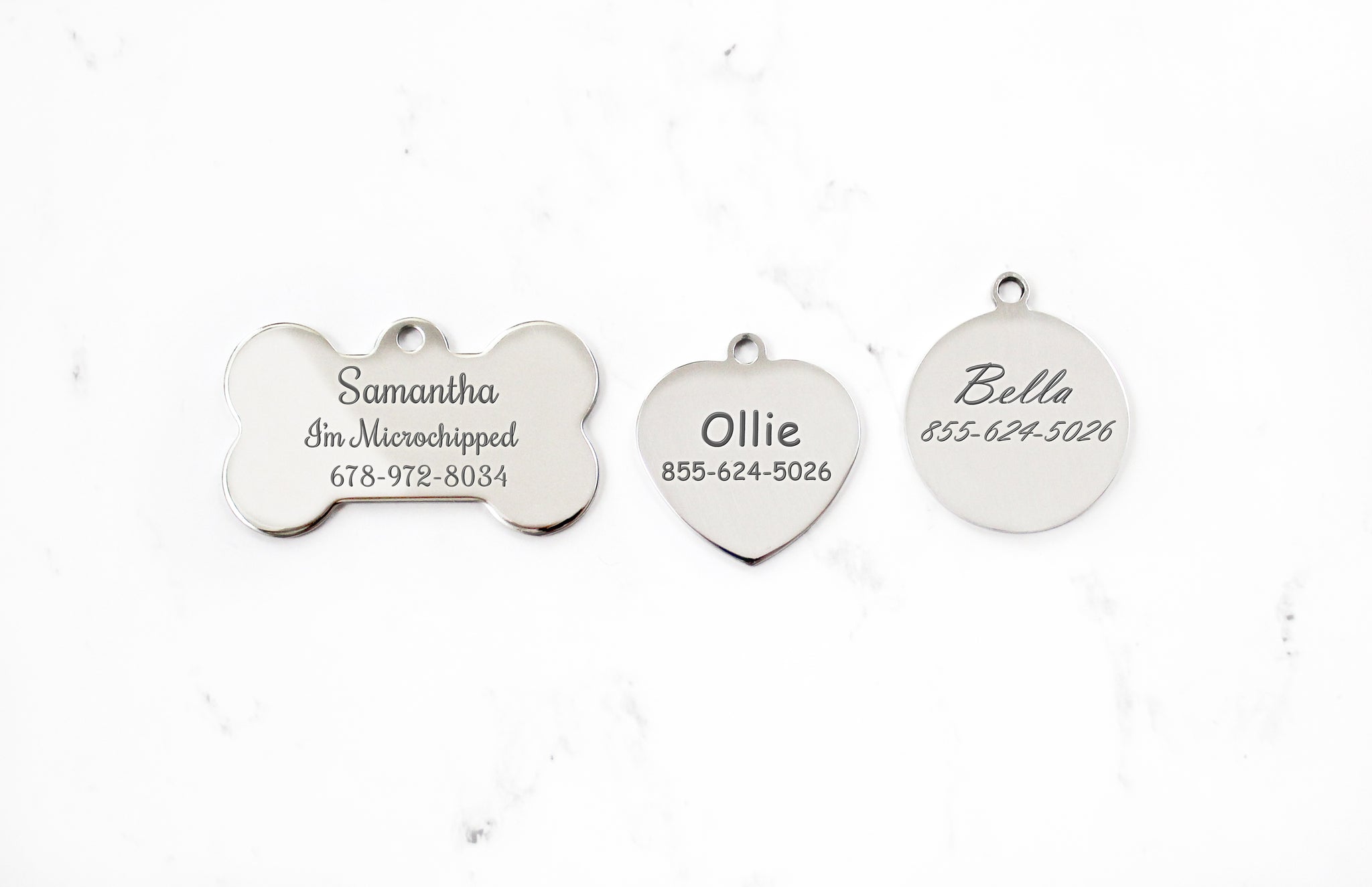 Engraved Silver Dog ID Tag with mirror finish in bone, heart and round shapes on a white marble background